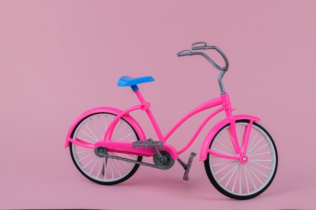 Hermosa bicicleta con sillín azul sobre fondo rosa.