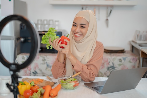 Una hermosa bloguera de comida musulmana asiática está transmitiendo en vivo en sus redes sociales en la cocina.