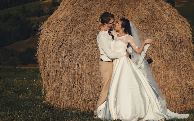 Hermosa boda en las montañas, una joven pareja feliz cerca del pajar.