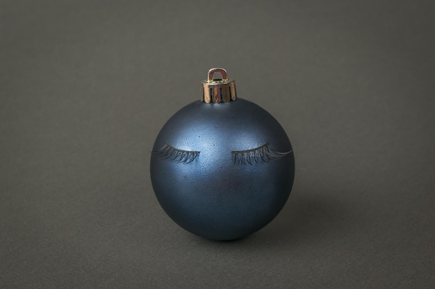 Una hermosa bola de árbol de Navidad azul con pestañas pegadas sobre un fondo gris oscuro. El concepto mínimo del Año Nuevo.