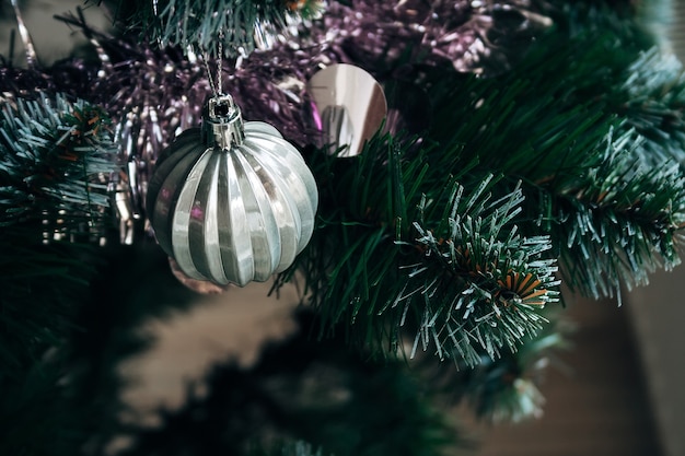 Hermosa bola de plata blanca y guirnalda rosa en árbol de Navidad artificial. Enfoque selectivo. Tarjeta navideña con adornos para la víspera de año nuevo.