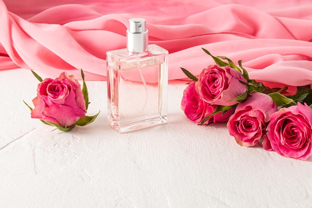 Hermosa botella de perfume de mujer o eau de parfum sobre un fondo de una bufanda de gasa rosa y rosas frescas Presentación de la fragancia