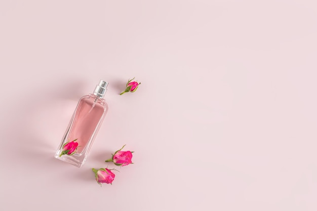 Una hermosa botella de perfume o spray para mujer sobre un fondo rosa con pequeños capullos de rosa Vista superior Un espacio de copia Presentación de la fragancia