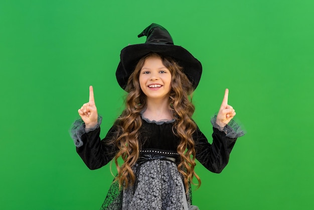 Una hermosa brujita señala con sus manos tu anuncio Una bruja con una capa negra y un sombrero sobre un fondo aislado