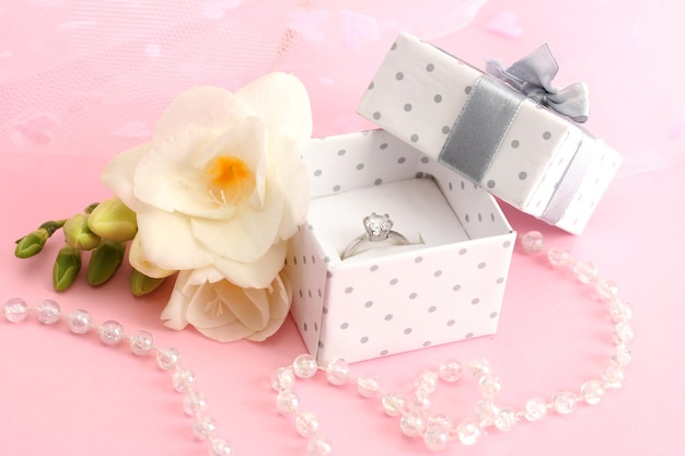 Hermosa caja con anillo de bodas y flor sobre fondo rosa