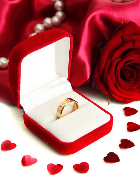 Hermosa caja con anillo de bodas y rosa sobre fondo de seda roja
