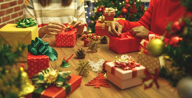 Hermosa caja de regalo empacada y envuelta por un grupo familiar de mujeres en un suéter con papel de colores, cinta, lazo encantador para decorar el árbol de Navidad de lujo para la preparación de la feliz fiesta de invierno en diciembre