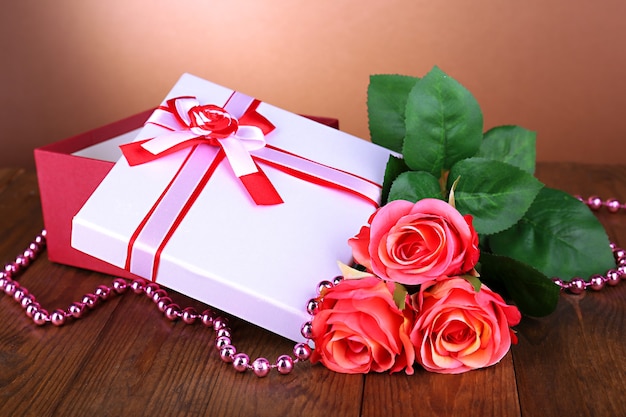 Hermosa caja de regalo con flores en la mesa sobre fondo marrón