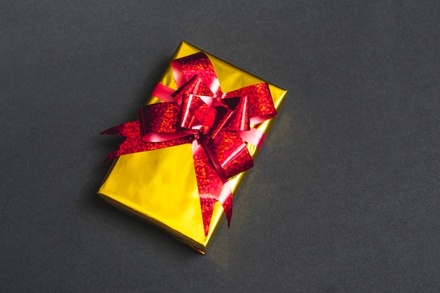 Hermosa caja de regalo de oro con un lazo rojo sobre un fondo negro de cerca, vista superior, con espacio de copia