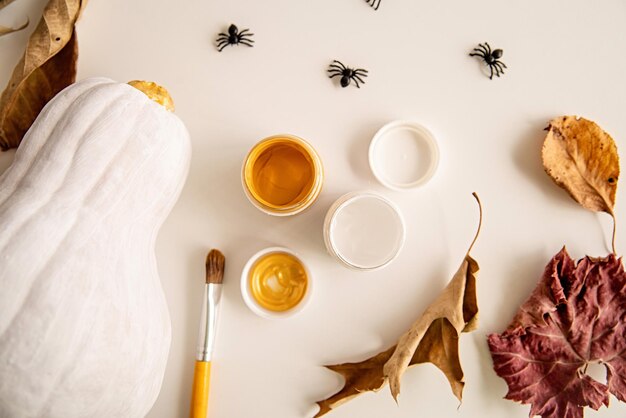 hermosa calabaza de Halloween pintada de blanco y oro en una mesa blanca decorada con arañas y hojas de otoño