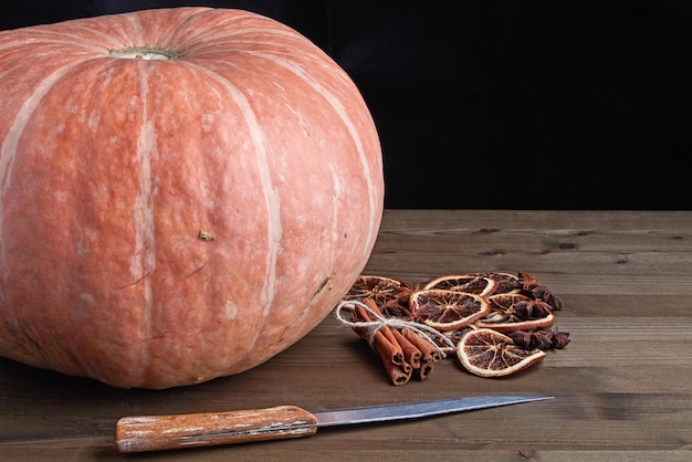 Hermosa calabaza naranja grande y especias secas para hacer mermelada en una mesa de madera sobre un fondo oscuro