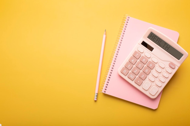 Hermosa calculadora de bloc de notas rosa y lápiz sobre un fondo amarillo con un lugar para una inscripción