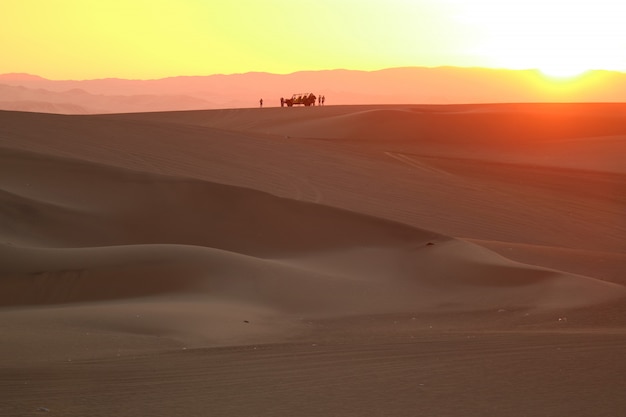 Hermosa capa de color de la puesta de sol sobre la duna de arena del desierto de Huacachina con la silueta de la duna holgada y la gente