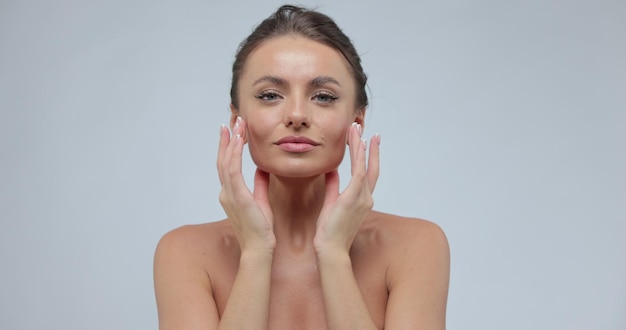 Hermosa cara de mujer mirando a la cámara aislada en el fondo gris del estudio Tratamiento para el cuidado de la piel o concepto de anuncios cosméticos