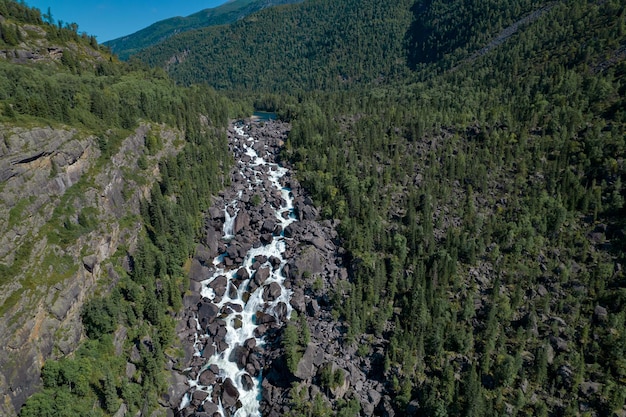 Una hermosa cascada que fluye a través de las colinas rocosas con muchos árboles diferentes bajo un cielo azul sin nubes.