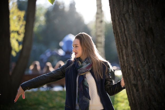 Hermosa chica en un abrigo al lado de un árbol en el parque soleado de otoño