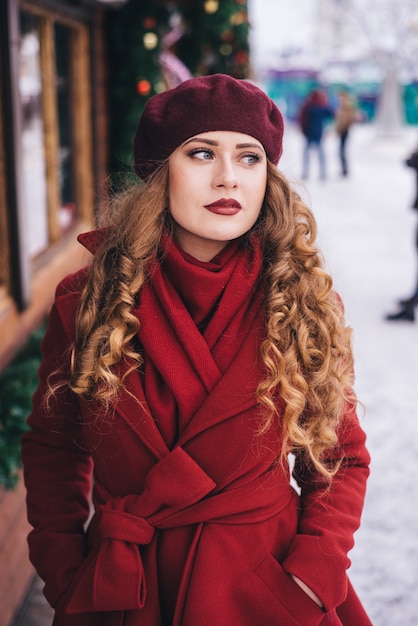 Hermosa chica con un abrigo rojo y una boina en la calle de Navidad