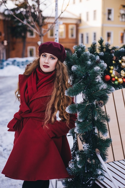 Hermosa chica con un abrigo rojo y una boina en la calle de Navidad