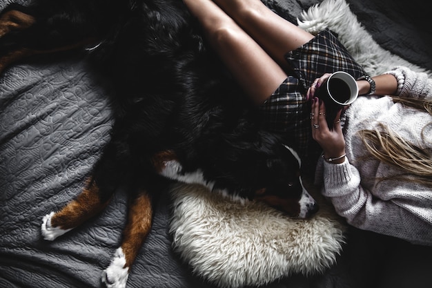 Hermosa chica acostada y su lindo perro Bernese Mountain Dog en la cama, elegante, de moda, acogedor