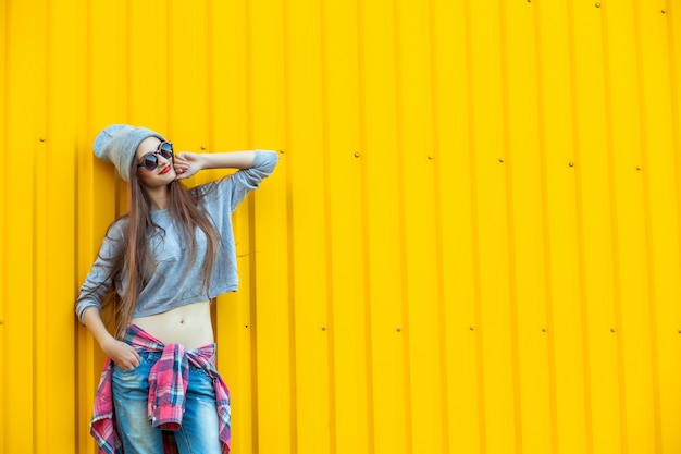 Hermosa chica adolescente de moda sobre pared amarilla