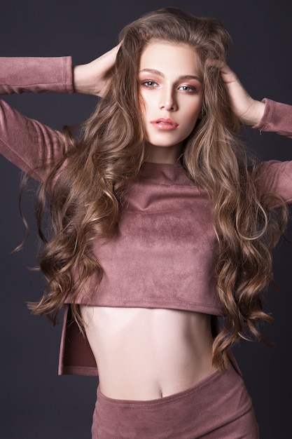 Hermosa chica adolescente con el pelo largo y ondulado posando en el estudio sobre un fondo negro, vestida con un traje de pana rosa. Concepto de moda