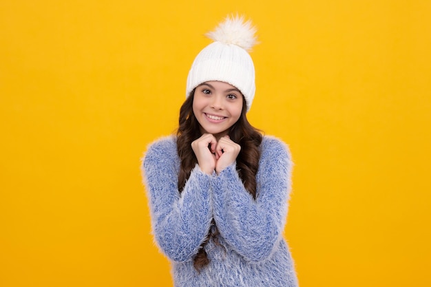 Hermosa chica adolescente en un sombrero de invierno y un suéter cálido Un niño sobre un fondo amarillo aislado Chica feliz cara emociones positivas y sonrientes