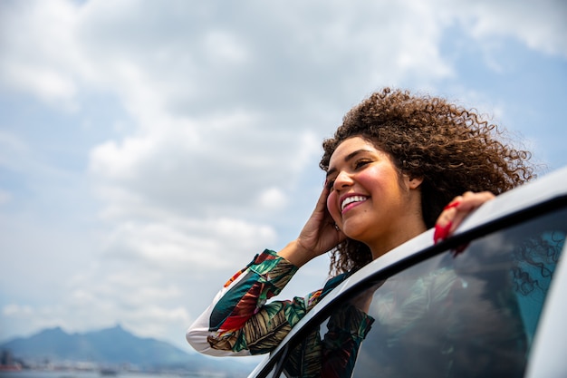 Hermosa chica afroamericana con un peinado afro lado sonriente de un auto