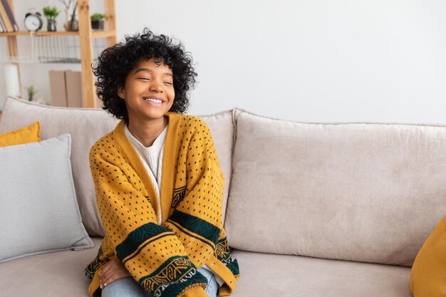 Hermosa chica afroamericana con peinado afro sonriendo sentada en un sofá en casa interior joven afr