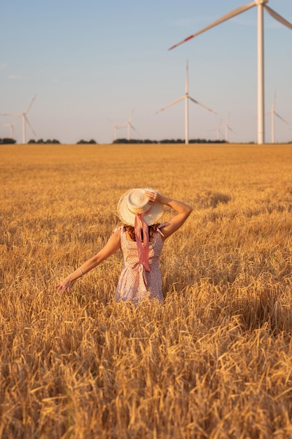 Hermosa chica al atardecer en un campo de trigo con molinos de viento para generar electricidad El concepto de energía renovable amor por la naturaleza electricidad Energía renovable