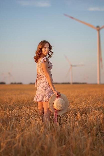 Hermosa chica al atardecer en un campo de trigo con molinos de viento para generar electricidad Concepto de energía renovable amor por la naturaleza electricidad Energía renovable