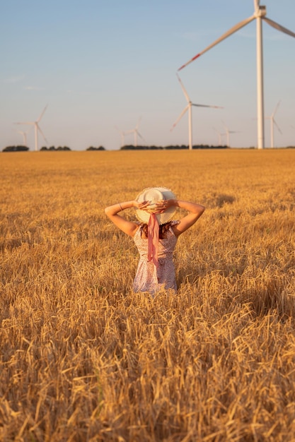 Hermosa chica al atardecer en un campo de trigo con molinos de viento para generar electricidad El concepto de energía renovable amor por la naturaleza electricidad Energía renovable