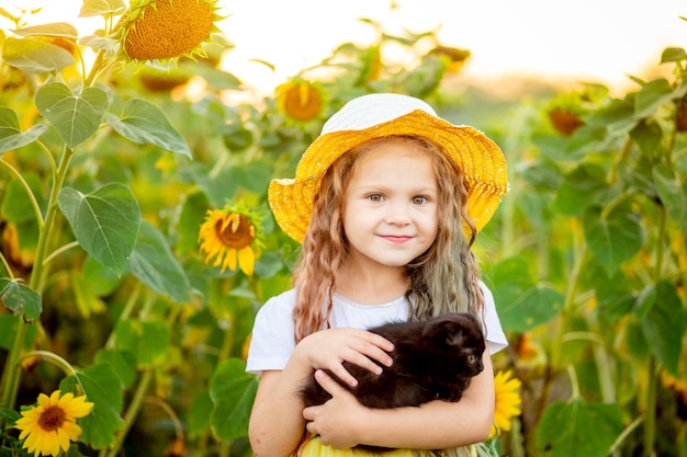 Hermosa chica alegre con un sombrero de paja en un campo amarillo con flores.