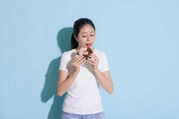 hermosa chica alegre sosteniendo deliciosos donuts sintiéndose feliz y de pie en el fondo de la pared azul lista para comer disfrutando del postre.