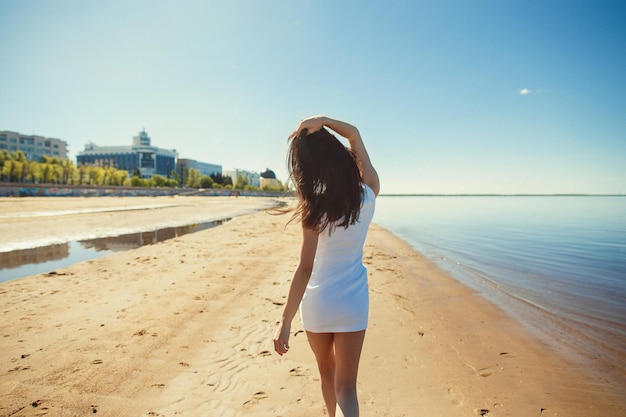 Foto una hermosa chica alta con cabello lujoso camina por la playa de la ciudad en un cálido día de verano