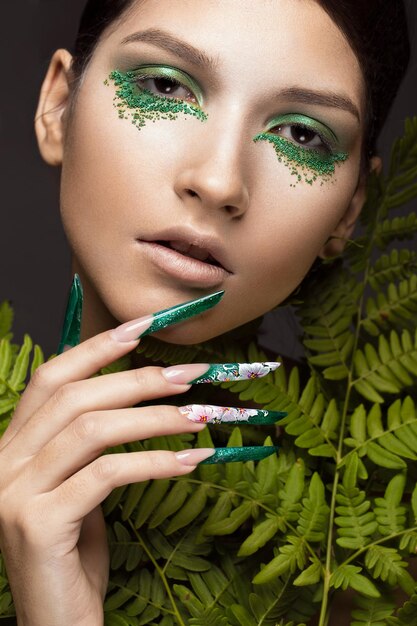 Hermosa chica con arte maquillaje hojas de helecho y uñas largas Diseño de manicura La belleza de la cara