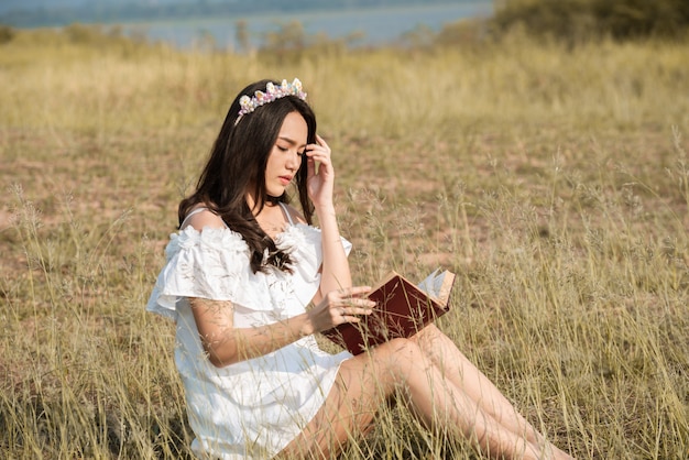 Hermosa chica de asia en el campo de hierba leyendo un libro cubierto