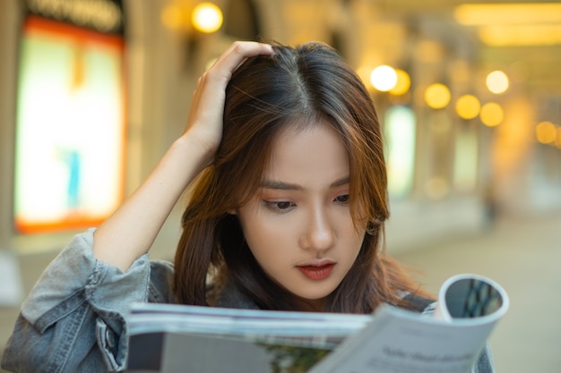 Hermosa chica asiática leyendo una revista en la calle