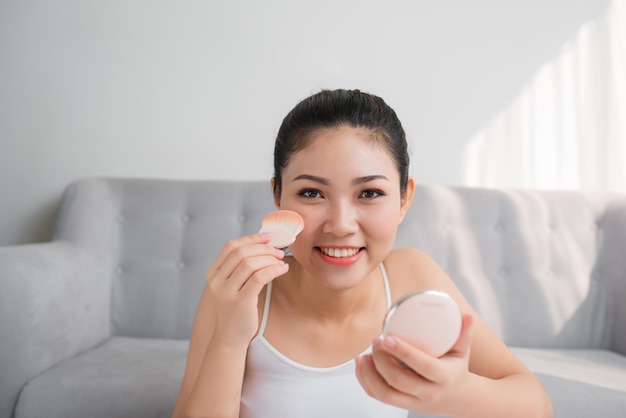 Hermosa chica asiática con pincel de polvo cosmético para maquillaje. Concepto de maquillaje