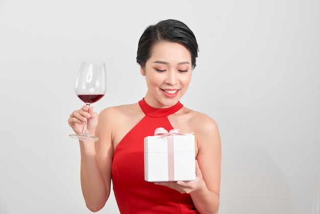 Hermosa chica asiática sexy sosteniendo una caja de regalo y una copa de champán y riendo.