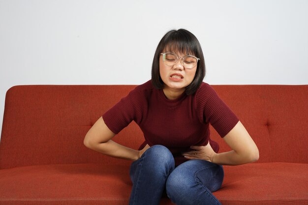 Hermosa chica asiática vestida con camisa roja y pantalones vaqueros azules tiene dolor de estómago dolor de estómago