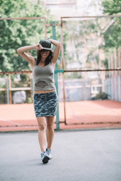 Hermosa chica atlética en ropa de color caqui y gorra en el patio de recreo. Estilo de vida saludable.