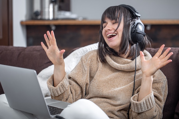 Hermosa chica en auriculares escuchando música en casa en el sofá con una computadora portátil.
