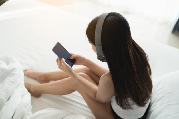 Hermosa chica con auriculares y teléfono móvil escuchando música en el dormitorio