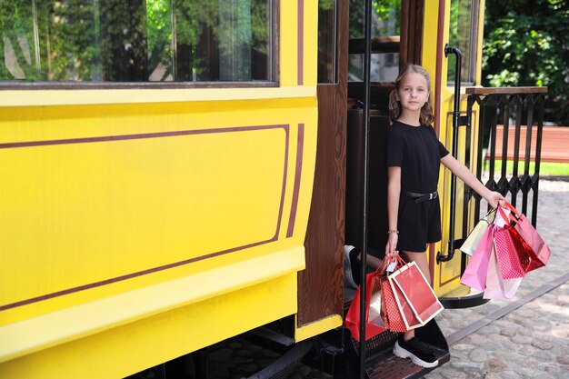 Hermosa chica se baja del tranvía con paquetes de colores en la ciudad