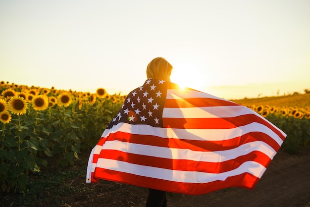 Hermosa chica con la bandera estadounidense en un campo de girasoles 4 de julio Libertad del 4 de julio