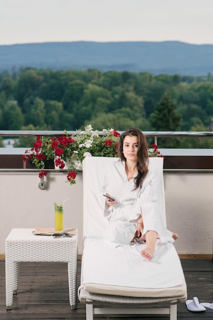 Hermosa chica en bata de baño relajarse en el balcón del hotel con hermosas vistas a las montañas