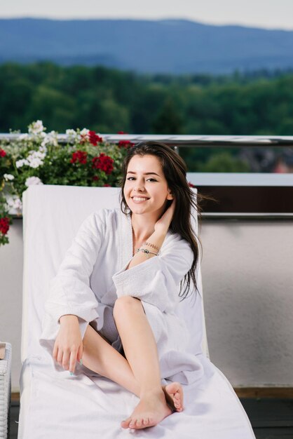 Hermosa chica en bata de baño relajarse en el balcón del hotel con hermosas vistas a las montañas