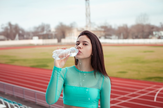 Hermosa chica bebe agua de una botella después del entrenamiento deportivo