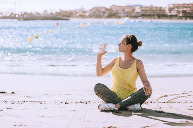 Foto hermosa chica bebe agua en la playa