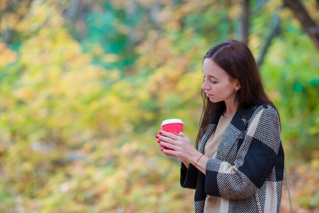 Hermosa chica bebiendo café caliente en otoño parque al aire libre